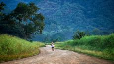 wide shot of a person running on a dirt road surround by tall grass and trees 